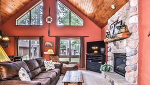 Una sala de estar acogedora con chimenea de piedra, sofá de cuero y ventanas amplias con vista a un jardín.