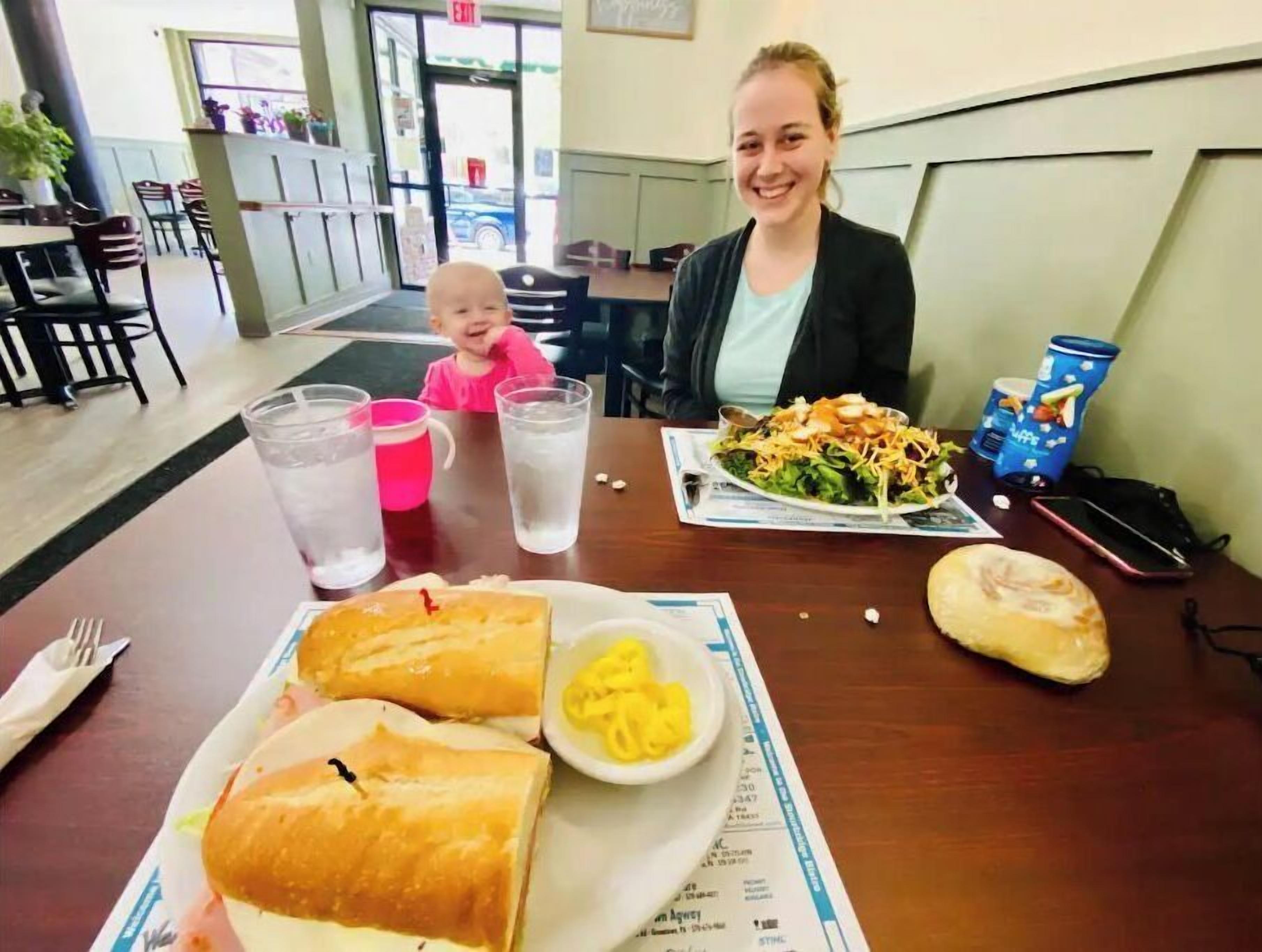 A restaurant interior with a dining table set for two, featuring a meal with bread, pasta, and a salad.