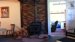 A living room with a brick fireplace, a chair, a table, and a painting on the wall.