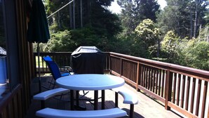 A deck with a round table and benches, surrounded by a wooden railing, overlooking a forested area.