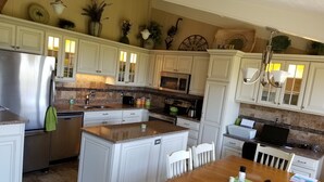 Una cocina amplia con muebles blancos, una isla central y un comedor con mesa y sillas de madera.