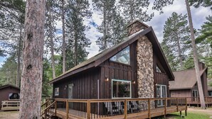 A cabin with a stone exterior, wooden deck, and large windows. - Elbert’s Resort lakeside cabin with dock and Timber’s bar and grill on site! (St.Germain)