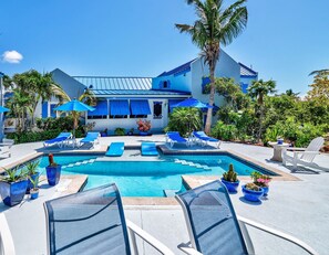 A pool area with lounge chairs and umbrellas, surrounded by palm trees and potted plants. - Grace Bay Beach Ocean Villas, Bougainvillea Villa. Rated #1 On Trip Advisor. (Providenciales)