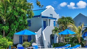 A pool area with blue umbrellas, lounge chairs, and potted plants.
