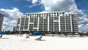 A multi-story hotel with a flat roof and numerous balconies, situated on a sandy beach with palm trees and beach chairs. - RI 410 Huge Double Shower! Beach Front! Popular Unit! Kitchen & Bath Upgrades (Orange Beach)