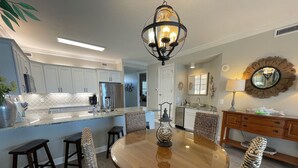 A modern kitchen with white cabinets, a stainless steel refrigerator, and a dining area with a round wooden table and wicker chairs. - RI 410 Huge Double Shower! Beach Front! Popular Unit! Kitchen & Bath Upgrades (Orange Beach)