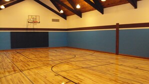 Un terrain de basket intérieur doté d’un plancher en bois, d’un panier de basket et d’un plafond haut avec des poutres apparentes.