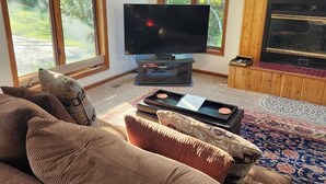 Un salon doté d’un grand téléviseur à écran plat, d’une cheminée et de grandes fenêtres donnant sur un paysage verdoyant.