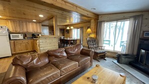 L’intérieur chaleureux d’un chalet avec un canapé en cuir, une table à manger en bois et un coin cuisine doté de meubles en bois et d’un four à micro-ondes.