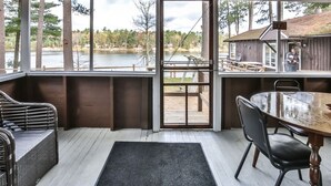 Un espace extérieur abrité, équipé d’une table et de chaises, d’un canapé en osier et offrant une vue sur un lac et des arbres.