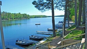 Une jetée au bord du lac, avec des bateaux, un escalier en bois et une rive bordée d’arbres.