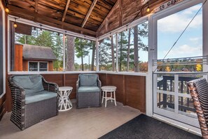 A covered outdoor seating area with wicker furniture and a view of trees and a building in the background. - Elbert’s Resort lakeside cabin with dock and Timber’s bar and grill on site! (St.Germain)
