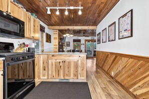 Una cocina con armarios de madera, microondas y estufa. Se aprecia una isla de madera con un lavaplatos y un comedor al fondo.