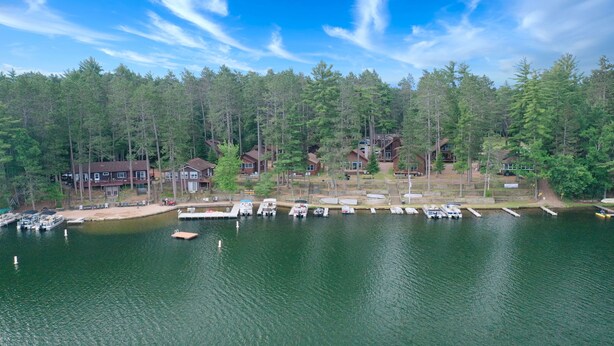 Une propriété au bord du lac, avec des bateaux amarrés, un quai et une forêt en arrière-plan.