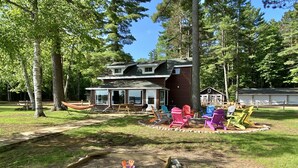 A cabin with a deck, surrounded by a playground with colorful Adirondack chairs and a sandbox. - Lakefront cabin on Lost Lake with dock and firepit next to bar and grill! (St. Germain)