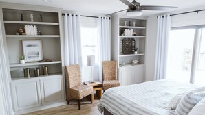 Ein Schlafzimmer mit einem Bett, zwei Korbstühlen, einem kleinen Tisch und eingebauten Regalen mit Dekoration.