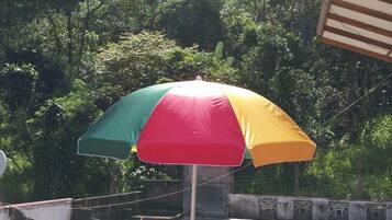Área de estar ao ar livre com mesa, cadeiras e um guarda-sol, com vista para uma paisagem verde exuberante.