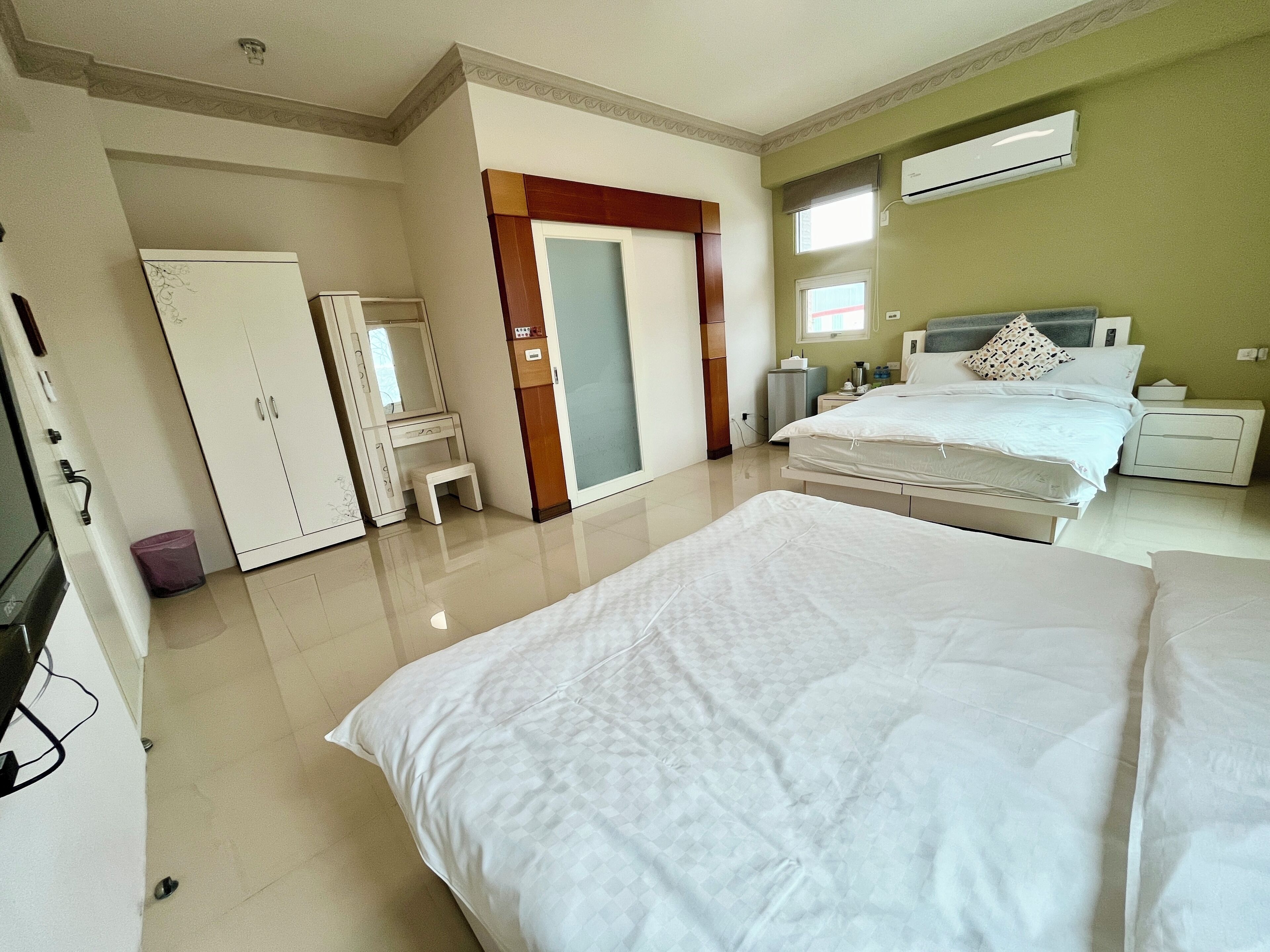 A hotel room with a bed, a desk, a wardrobe, a mirror, and an air conditioning unit.