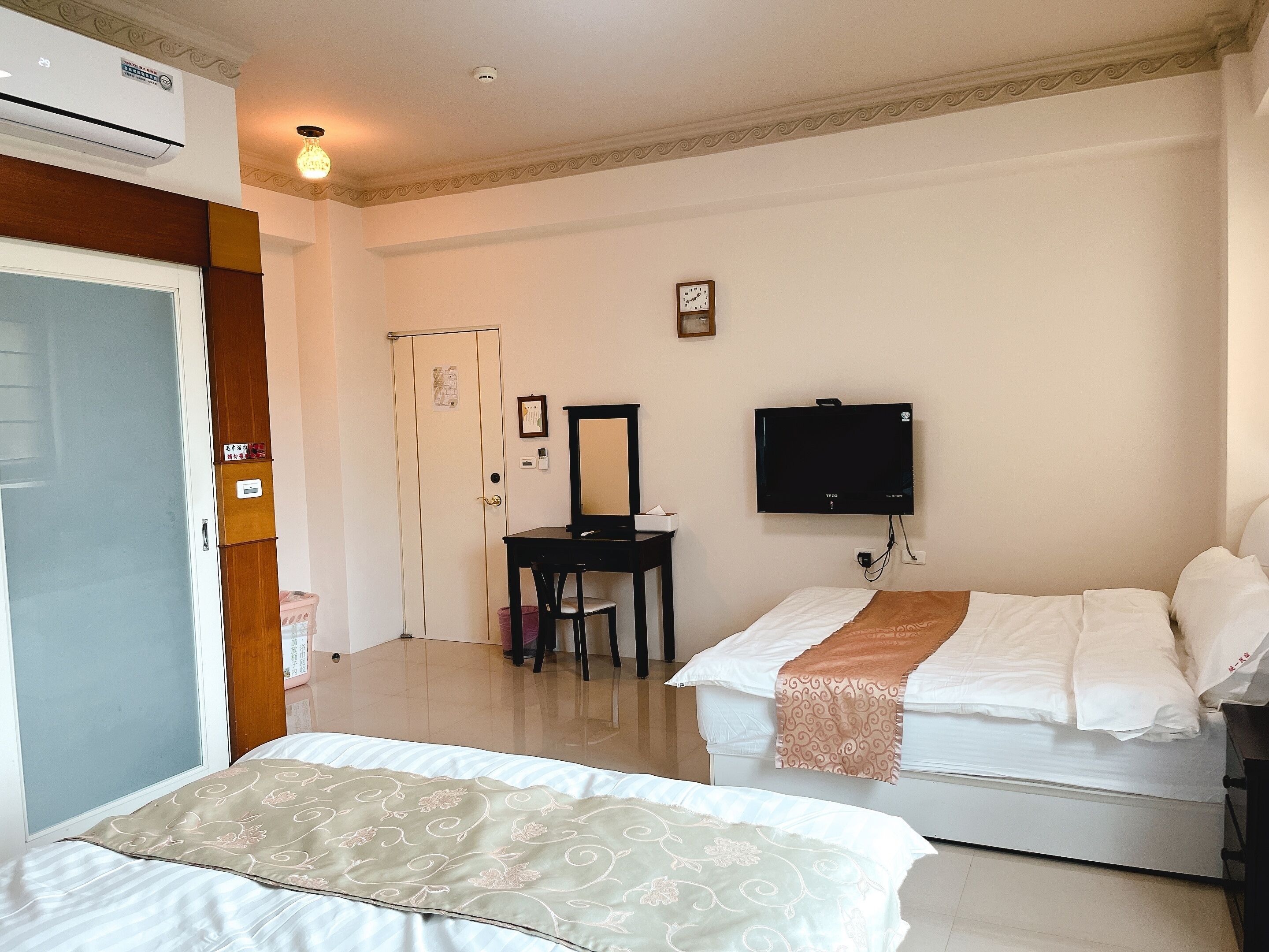 Una habitación de hotel con cama, escritorio con silla, televisor y aire acondicionado.