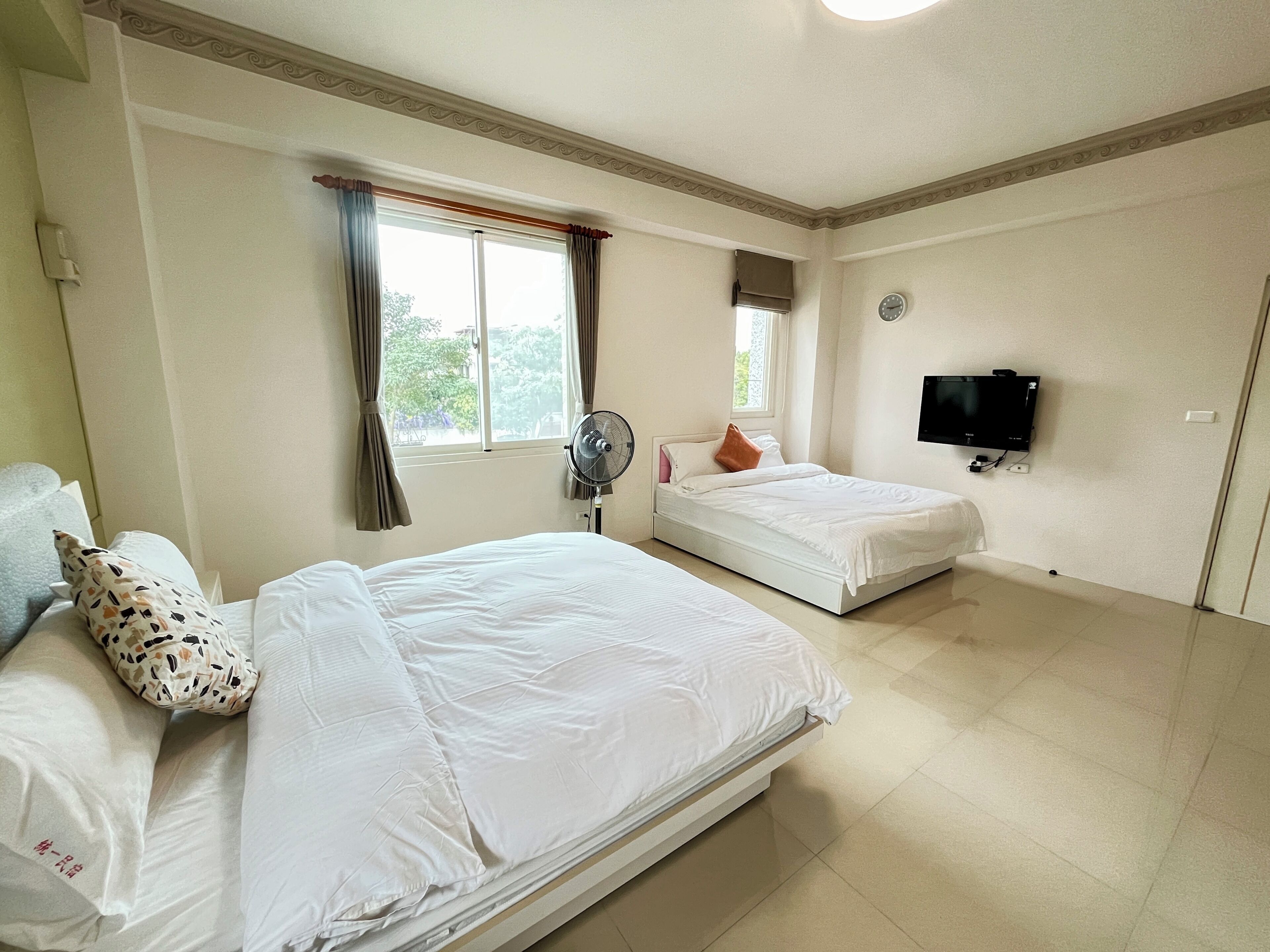 A hotel room with two beds, a TV, and a window with curtains.