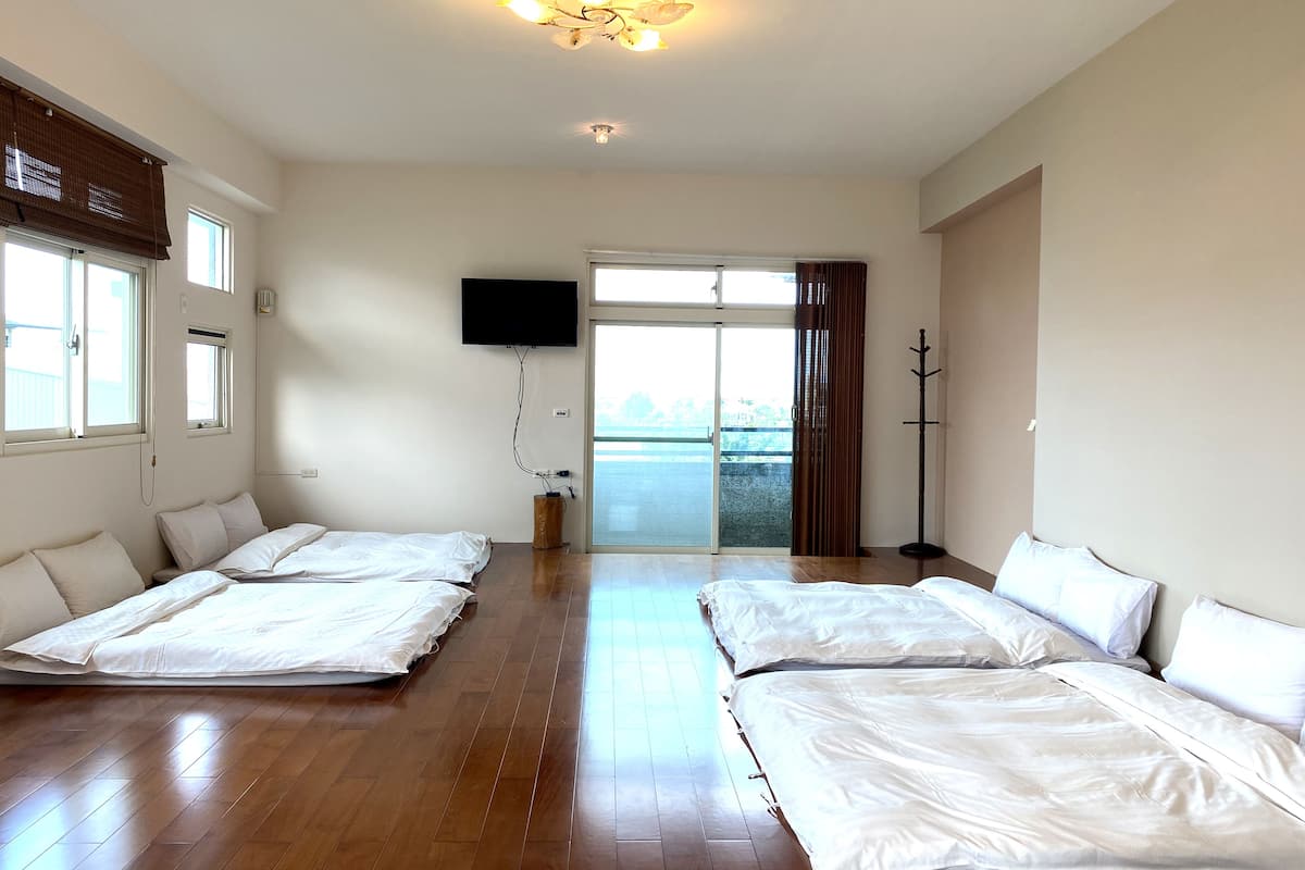 Quarto de hotel com duas camas, televisão, porta de vidro deslizante para a varanda e piso de madeira.