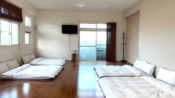 Habitación de hotel con dos camas, televisión, puerta corredera de vidrio al balcón y suelo de madera.
