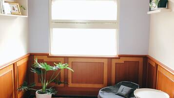 A corner room with a large window, a potted plant, a grey bean bag chair, a small white table, and a colorful rug.