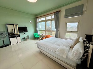 A hotel room with a bed, a desk, a chair, a TV, a fan, and a window with curtains. - TONG YI Homestay (Ji'an)