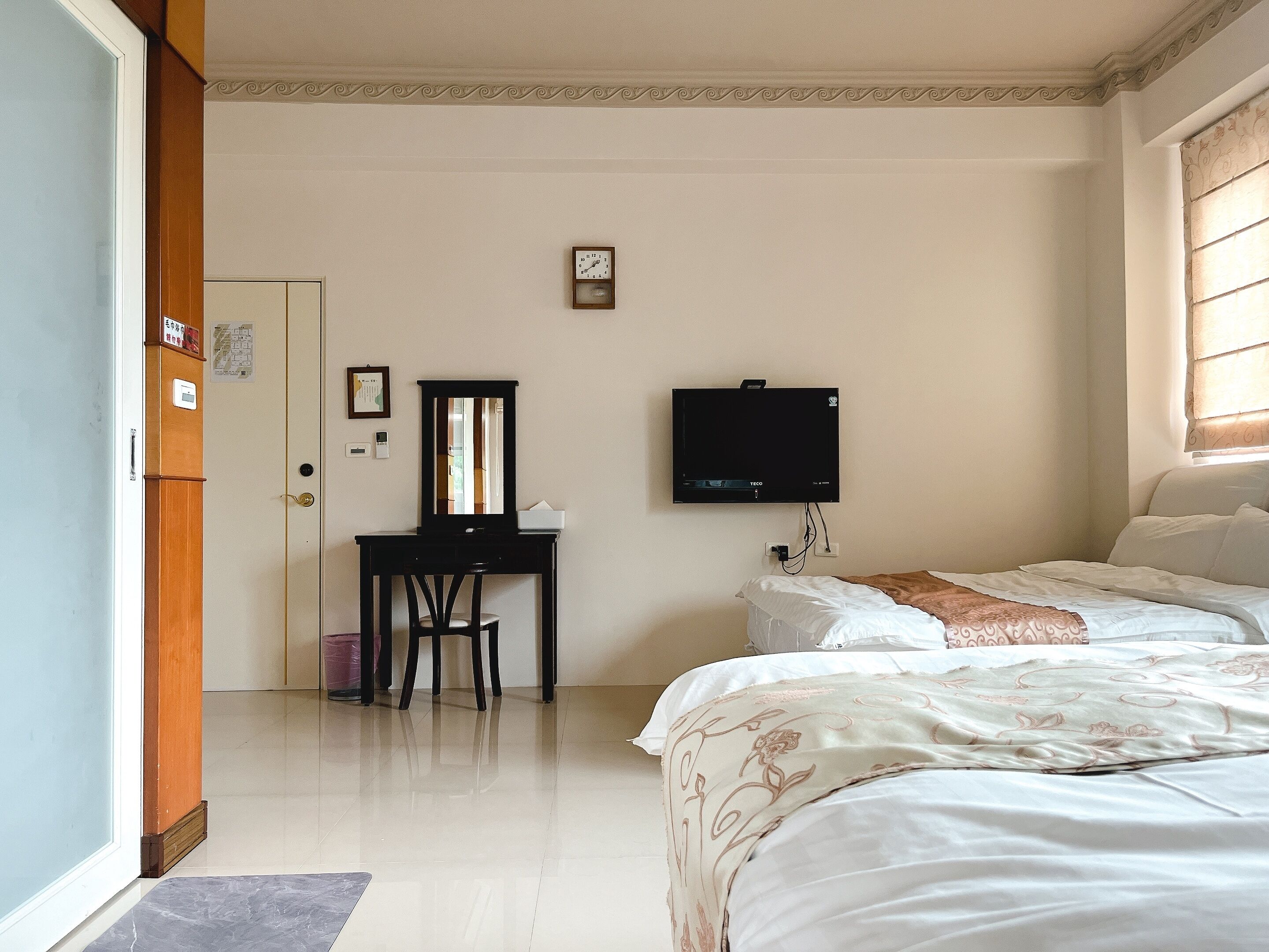 Habitación de hotel con cama, escritorio con silla, televisor y ventana con persianas.