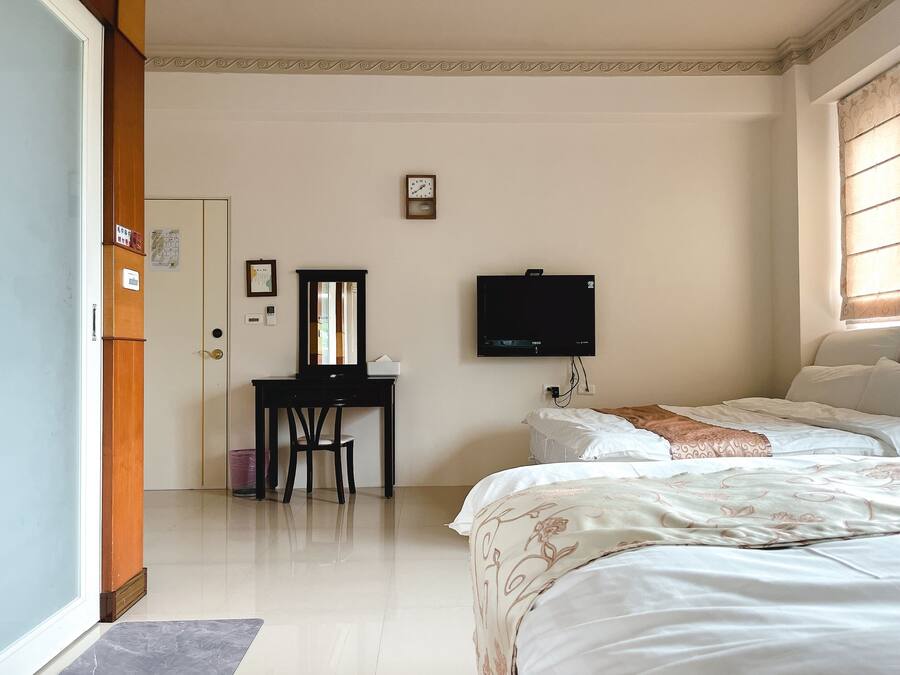 Habitación de hotel con cama, escritorio con silla, televisor y ventana con persianas.