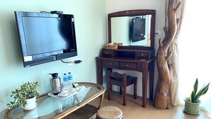 A hotel room with a flat-screen TV, a wooden vanity with a mirror, a glass coffee table, a wicker chair, and a potted plant. - TONG YI Homestay (Ji'an)