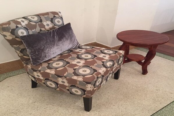 Un sillón estampado con un cojín oscuro y una mesita de madera cerca.