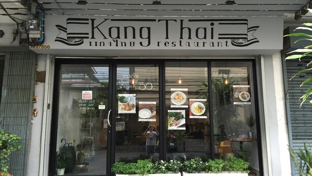 Ein Restaurant namens 'Kang Thai' mit einer Glasfassade, die Essensbilder zeigt.