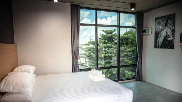 Une chambre d’hôtel moderne avec une grande fenêtre, un lit bien fait et une vue sur les arbres.