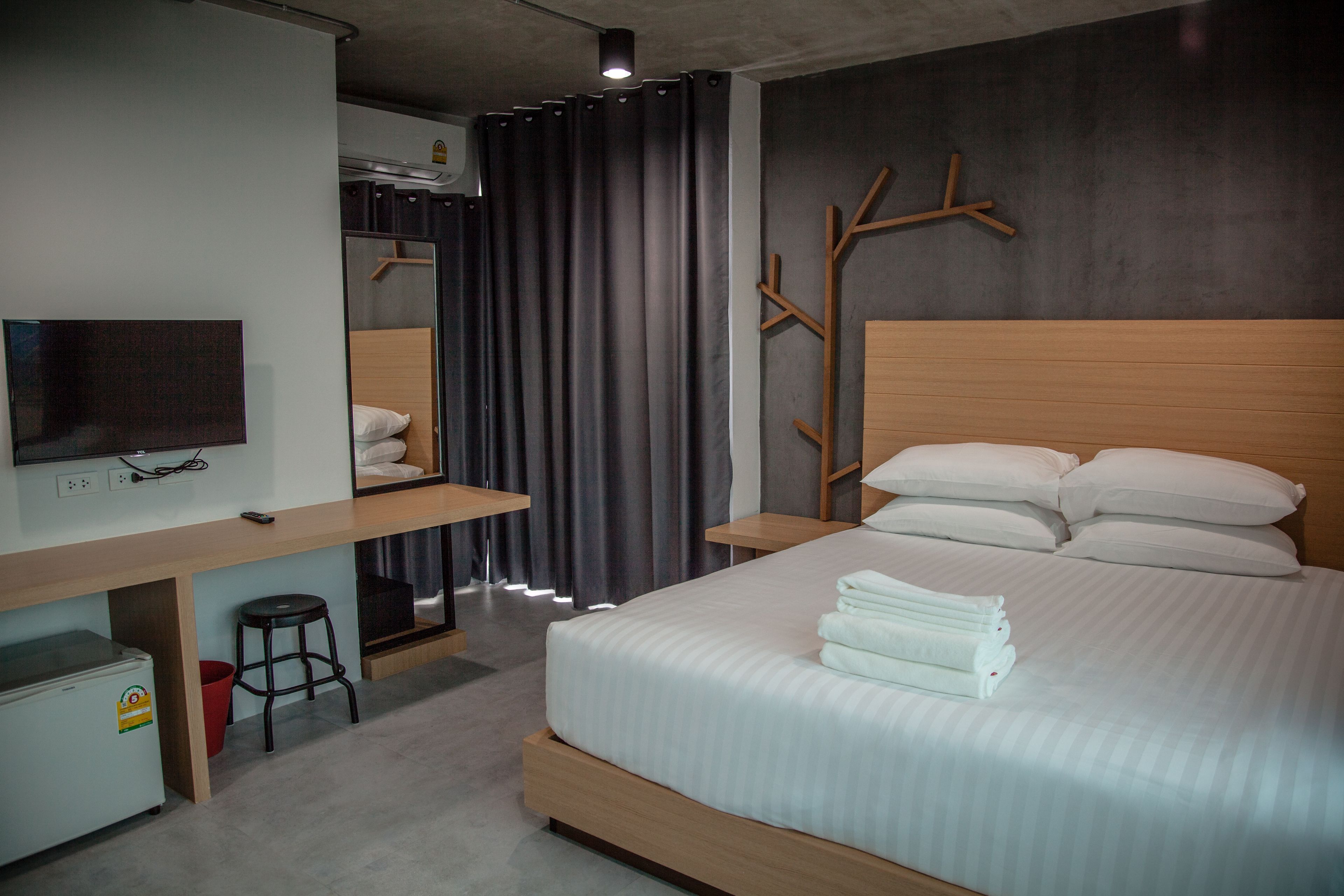A modern hotel room with a bed, a desk with a television, a wardrobe, and a mirror.