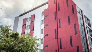 Un hôtel moderne, avec une façade rouge et blanche bien visible, de grandes fenêtres et un logo clairement affiché en haut.