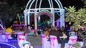 Um espaço para eventos ao ar livre decorado, com uma estrutura em arco branca, mesas e cadeiras.