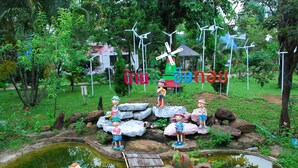 Um jardim com lago, turbinas eólicas e estátuas de crianças.