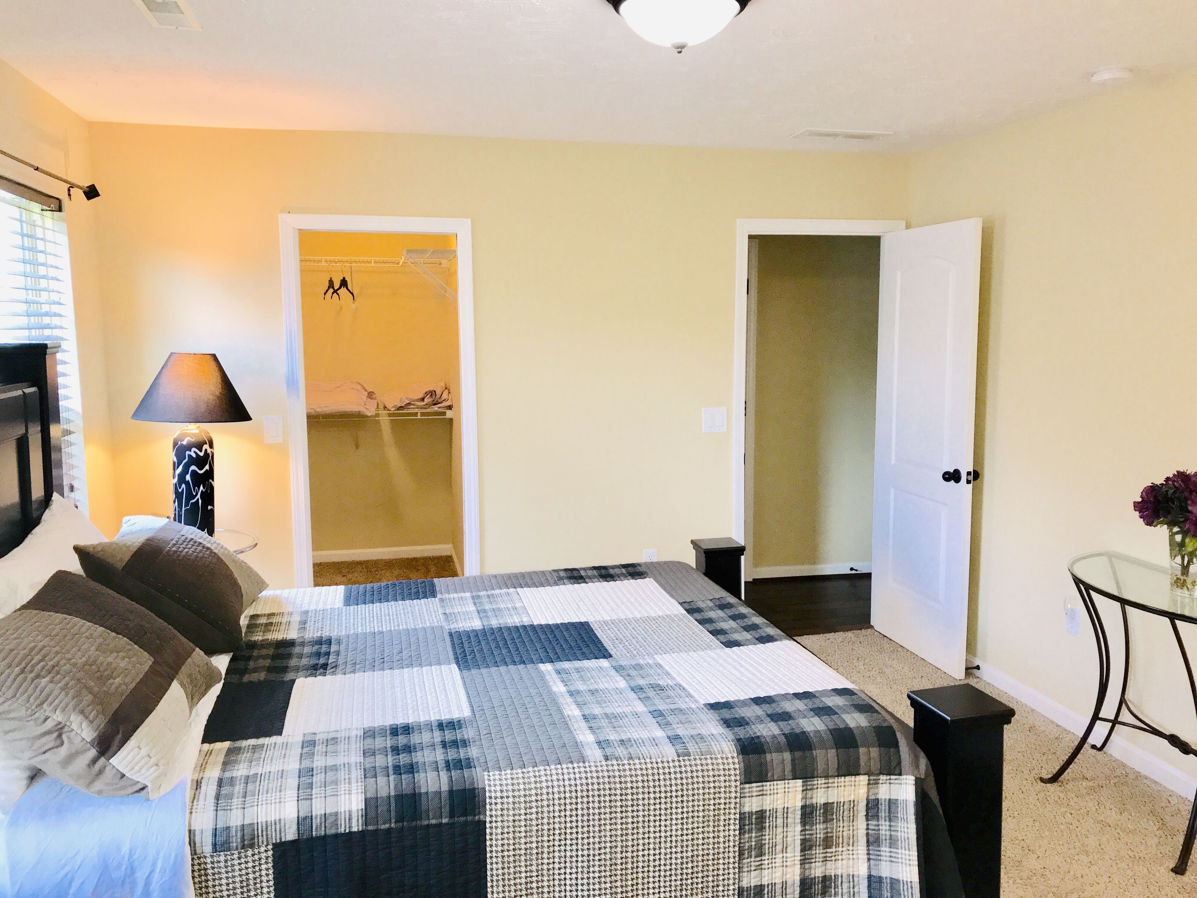 A bedroom with a large bed, a bedside lamp, a small table with flowers, and two doors leading to other rooms.