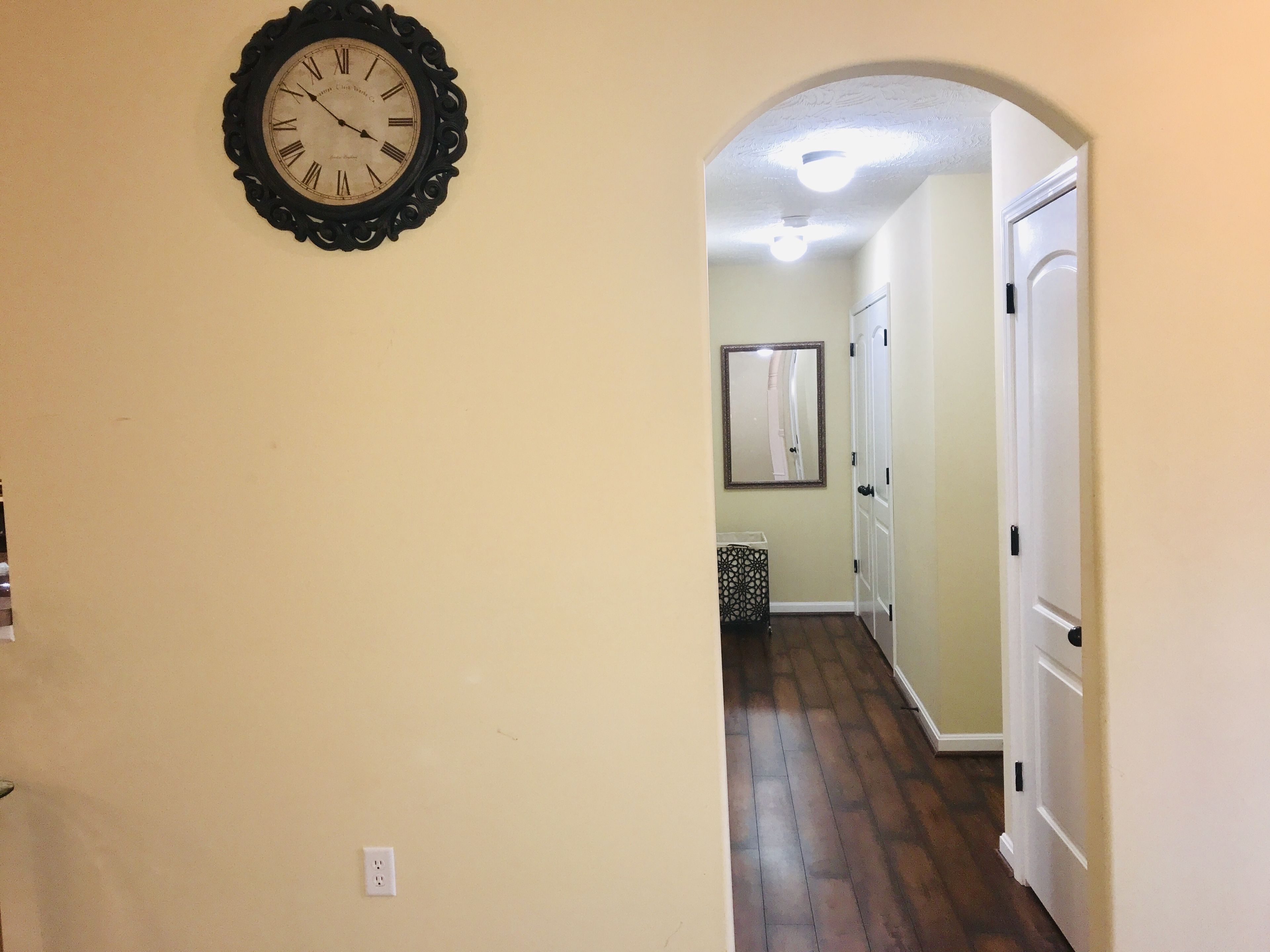 A hallway with a wall-mounted clock, a door, and a small table with a decorative item.