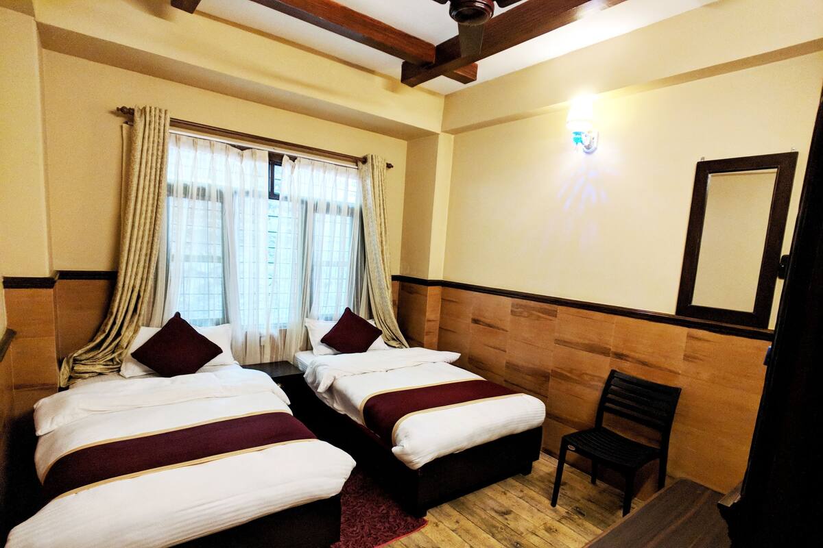 A hotel room with two beds, a wooden floor, a chair, and a mirror on the wall.