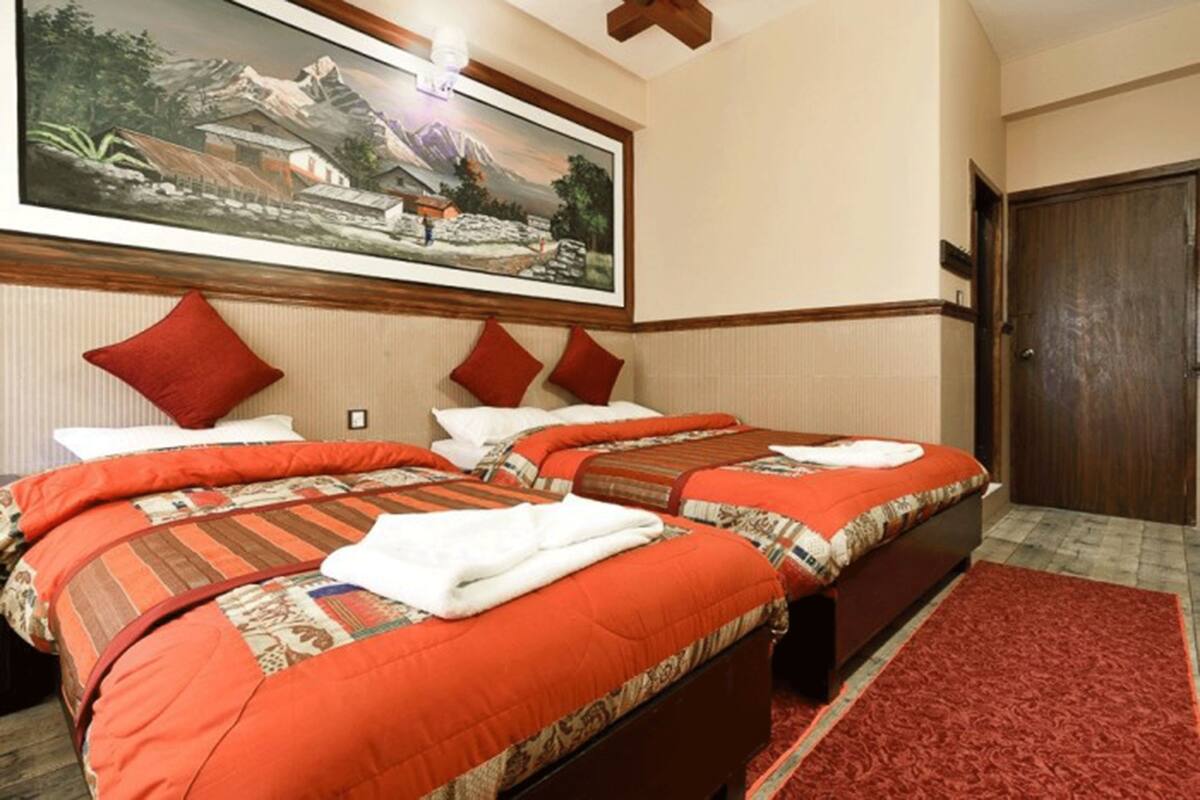A hotel room with two beds, a red rug, and a painting of a mountainous landscape.