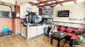 A reception area with a wooden reception desk, a sofa with red cushions, and a wall displaying various service options. - Hotel Forest Lake Backpackers' Hostel (Pokhara)