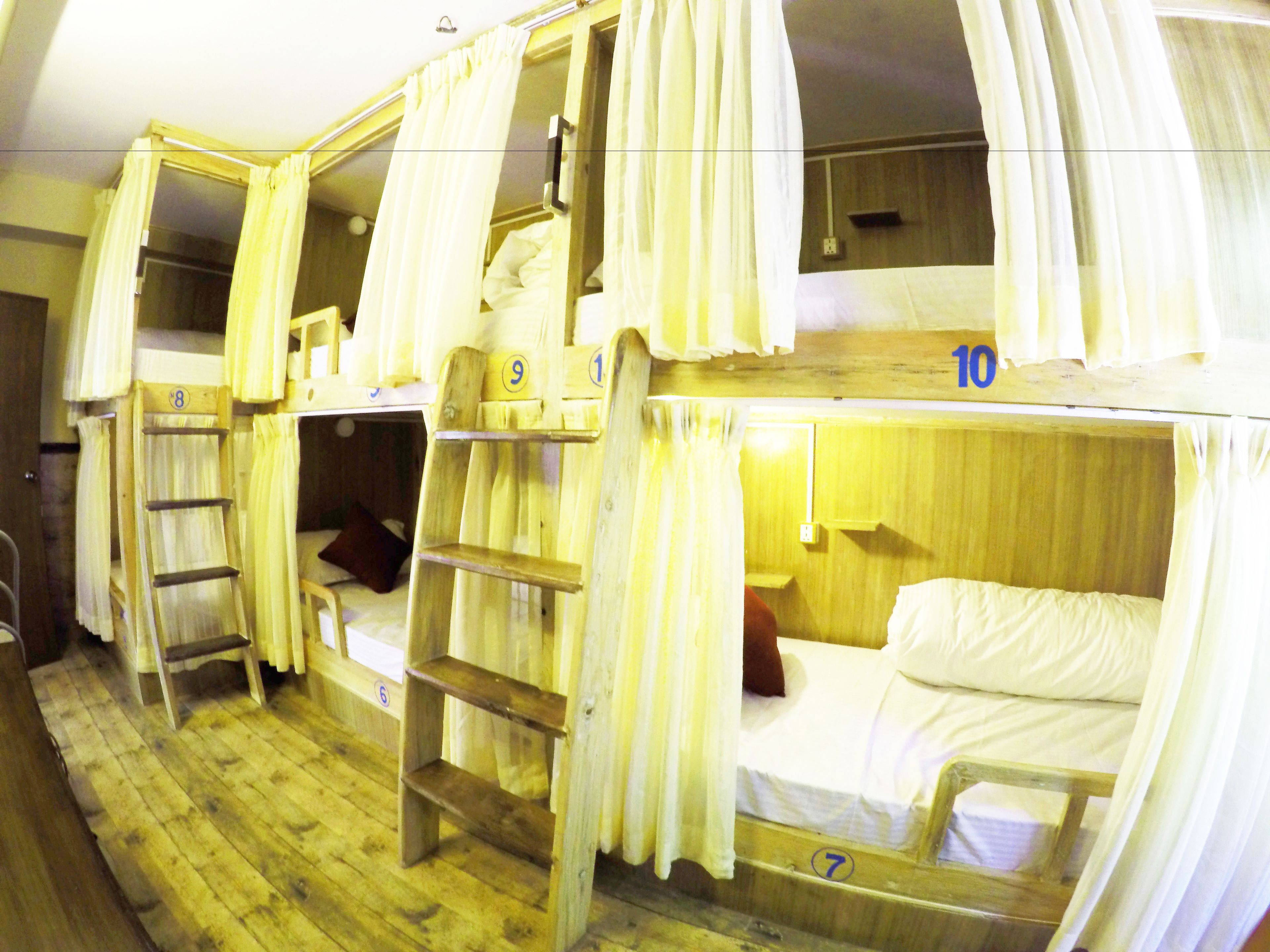 A row of bunk beds with curtains, wooden ladders, and numbered beds.
