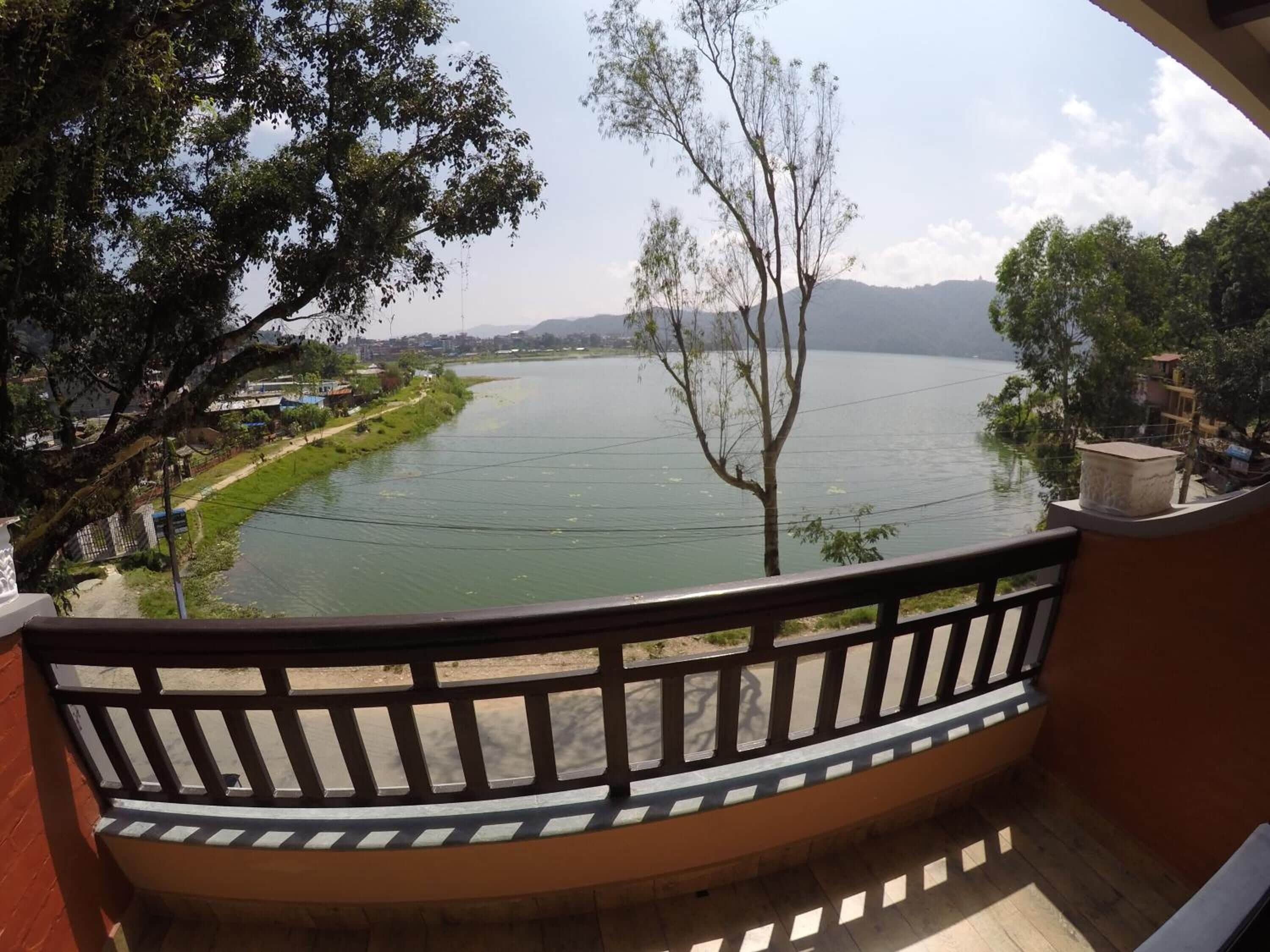 A balcony with a view of a river, trees, and distant hills.