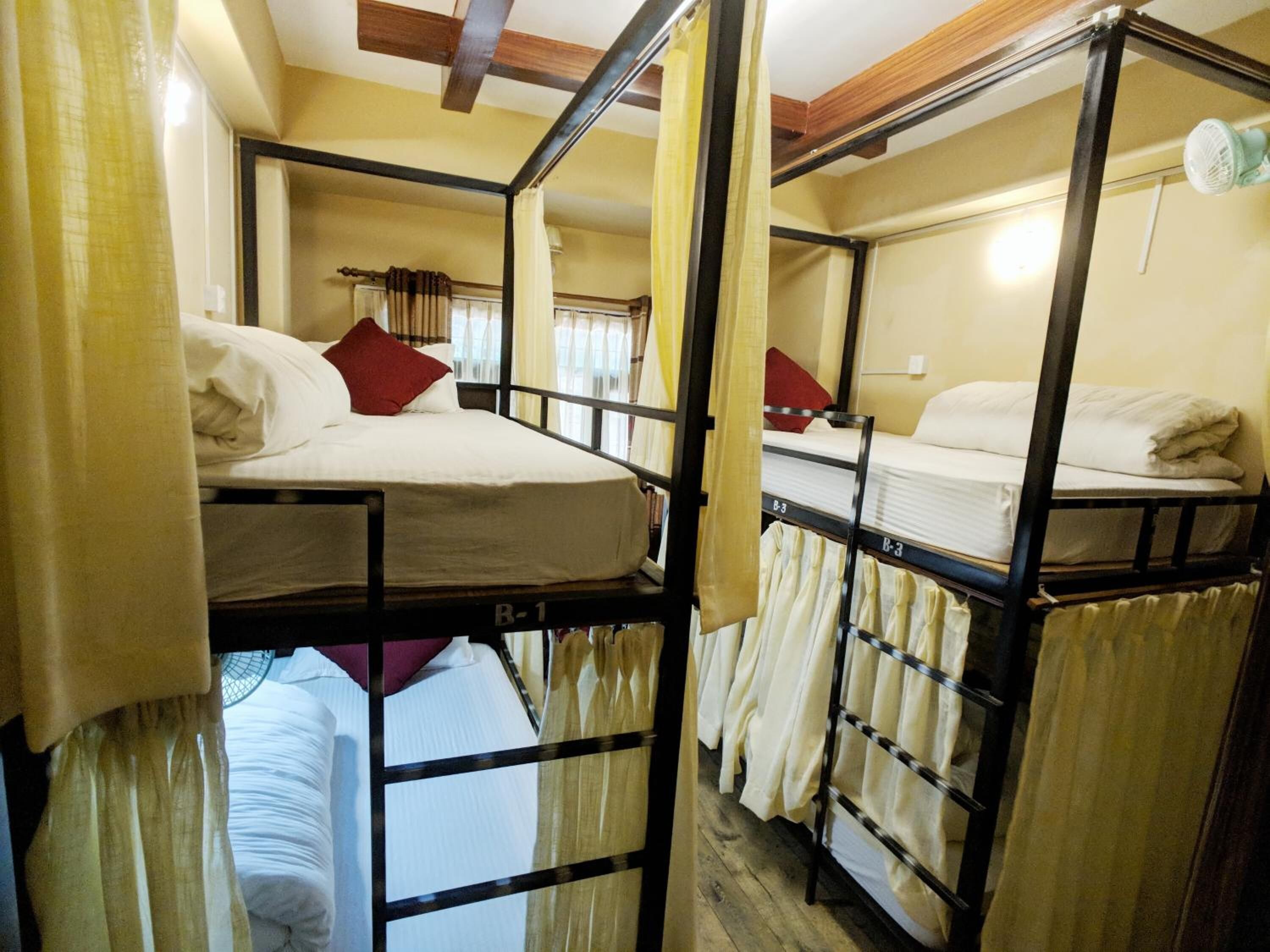 Quarto de dormitório com beliches, cortinas e um ventilador.