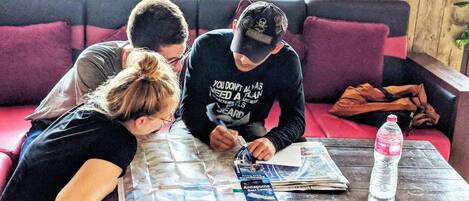 Three people sitting on a red couch, one person writing on a map, and a bottle of water on a wooden table.
