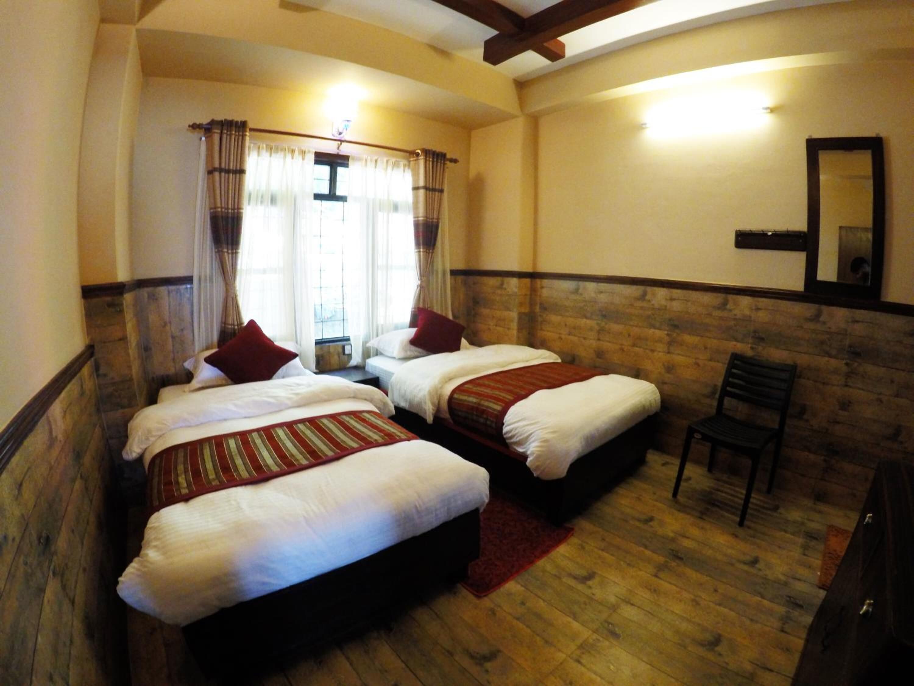 A room with two single beds, a wooden floor, a red rug, a wooden bench, and a mirror on the wall.