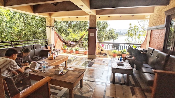 A covered outdoor seating area with tables and chairs, surrounded by potted plants and a hammock. - Hotel Forest Lake Backpackers' Hostel (Pokhara)