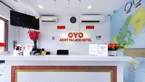 Un mostrador de recepción en el Hotel OYO Adiff Palace con un mapa del mundo, relojes y un letrero que indica WiFi gratuito.